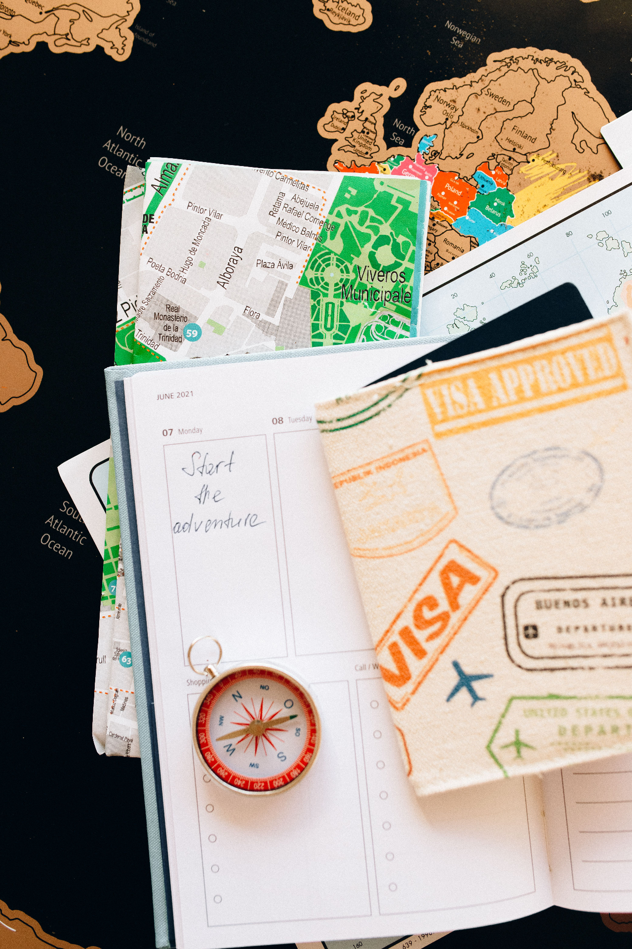 Passport with visa stamps, a compass and a world map laid out on a travel planner