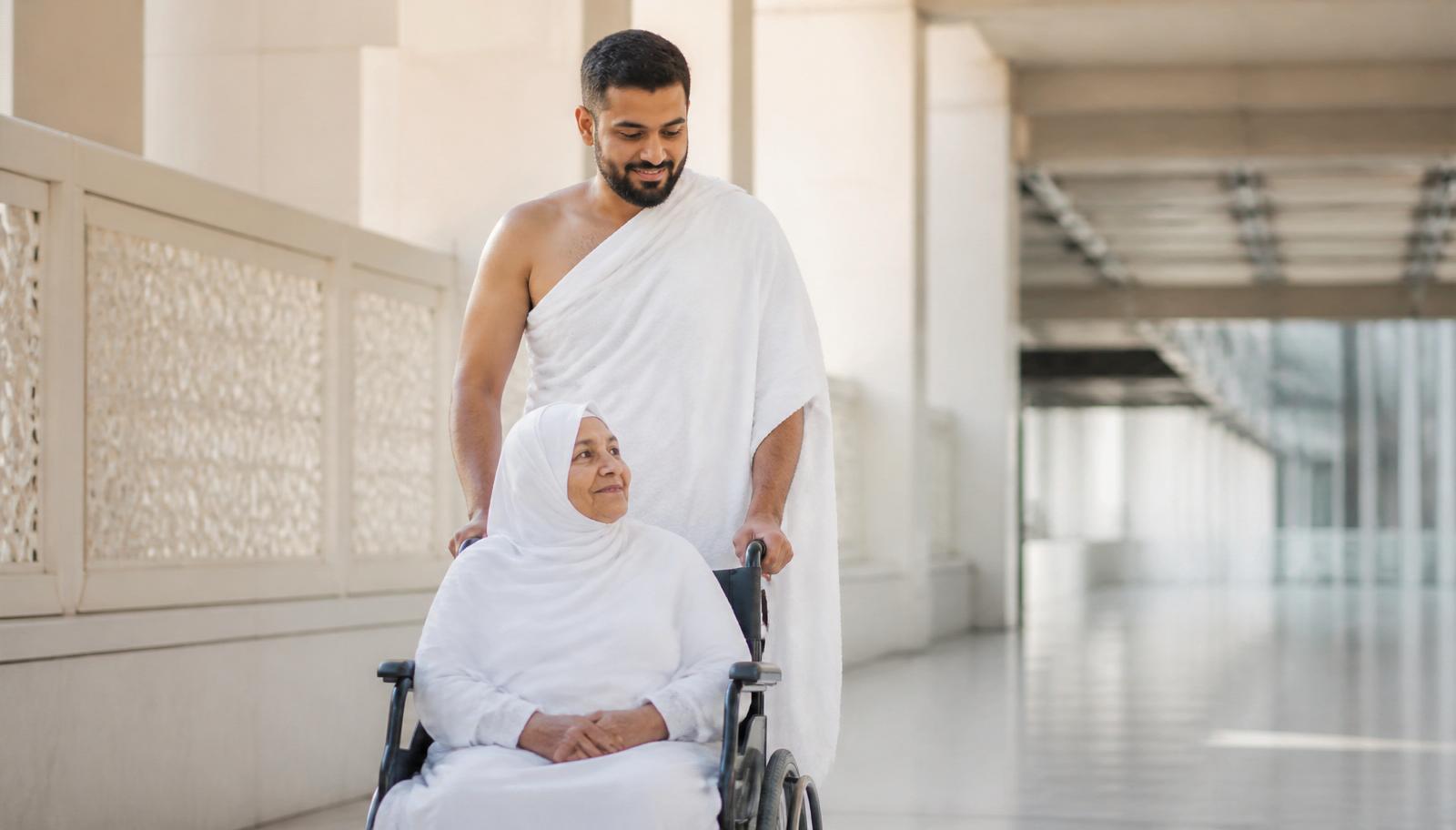 Pilgrim in Ihram assisting an elderly lady in a wheelchair